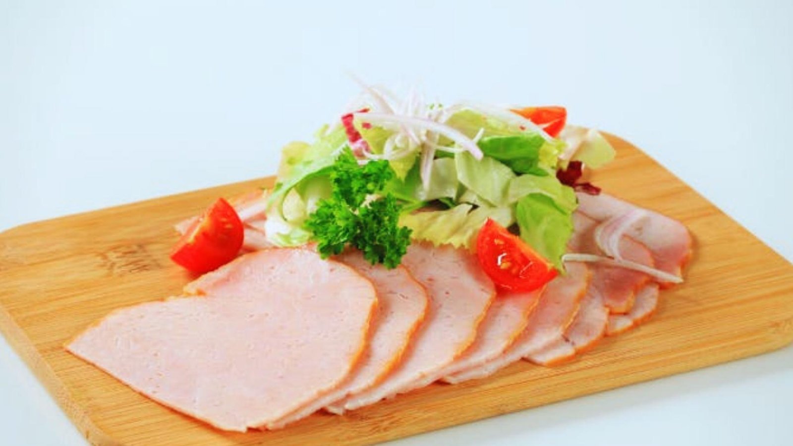 Thinly sliced turkey breast arranged on wooden cutting board with fresh lettuce, tomato wedges, red onion, and parsley garnish.